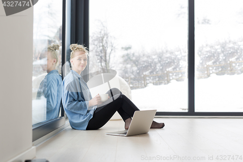 Image of woman drinking coffee and using laptop at home