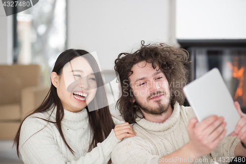 Image of multiethnic couple using tablet computer in front of fireplace