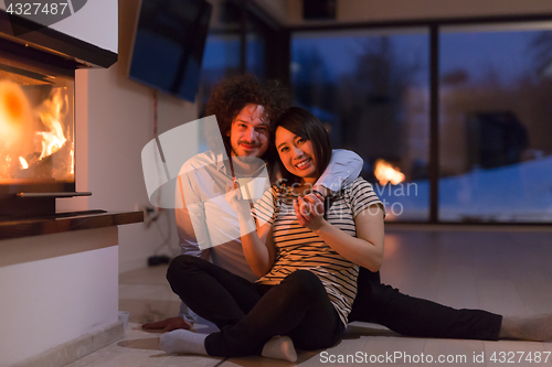 Image of happy multiethnic couple sitting in front of fireplace