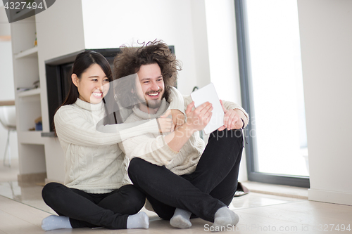 Image of multiethnic couple using tablet computer in front of fireplace