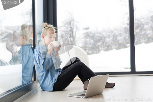 Image of woman drinking coffee and using laptop at home