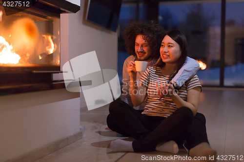 Image of happy multiethnic couple sitting in front of fireplace