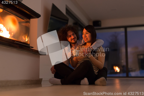 Image of happy multiethnic couple sitting in front of fireplace