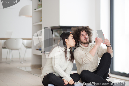Image of multiethnic couple using tablet computer in front of fireplace