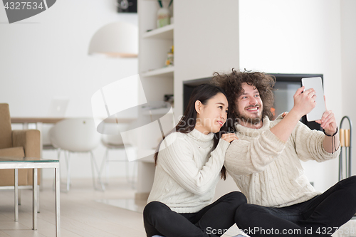 Image of multiethnic couple using tablet computer in front of fireplace