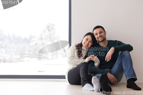 Image of multiethnic couple sitting on the floor near window at home