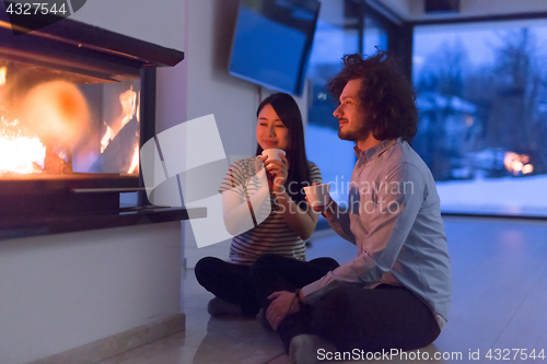 Image of happy multiethnic couple sitting in front of fireplace