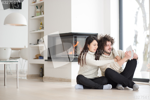 Image of multiethnic couple using tablet computer in front of fireplace