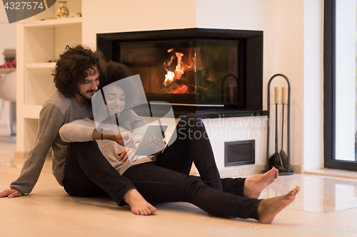 Image of multiethnic couple using tablet computer on the floor