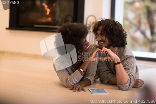 Image of multiethnic couple showing a heart with their hands on the floor