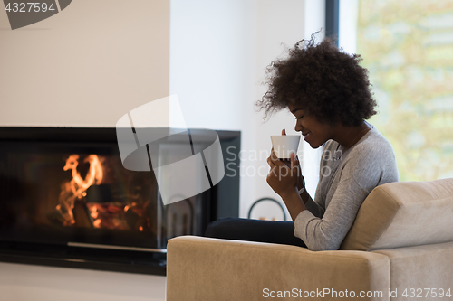 Image of black woman drinking coffee in front of fireplace