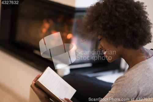 Image of black woman reading book  in front of fireplace