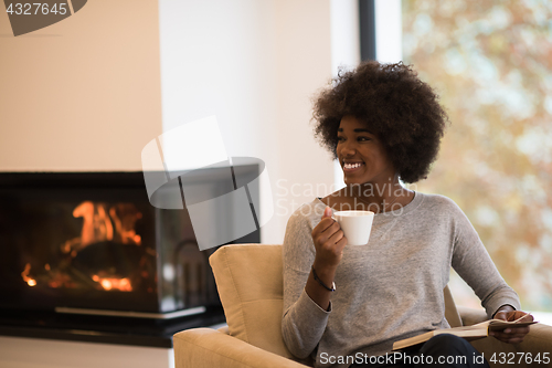 Image of black woman reading book  in front of fireplace