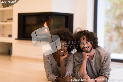 Image of multiethnic couple lying on the floor  in front of fireplace