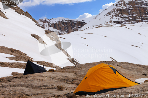 Image of Two camping tents on rocks in snow mountains at evening