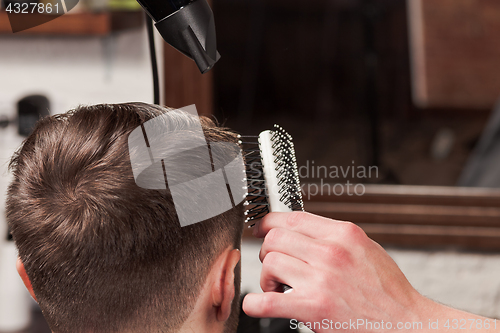 Image of The hands of barber making haircut to young man in barbershop