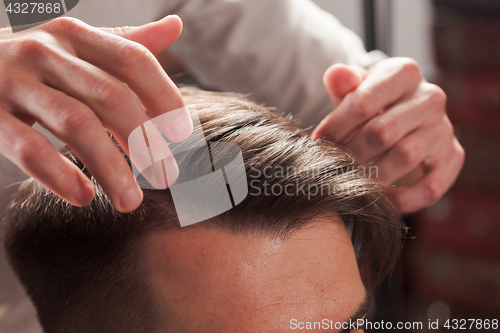 Image of The hands of barber making haircut to young man in barbershop
