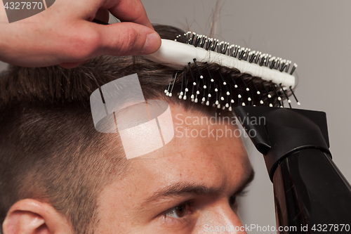 Image of The hands of barber making haircut to young man in barbershop