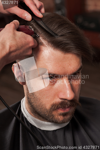 Image of The hands of barber making haircut to young man in barbershop