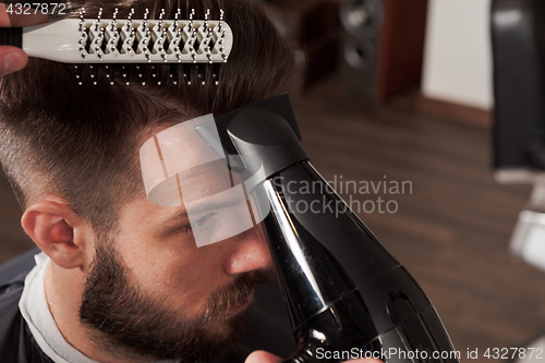 Image of The hands of barber making haircut to young man in barbershop