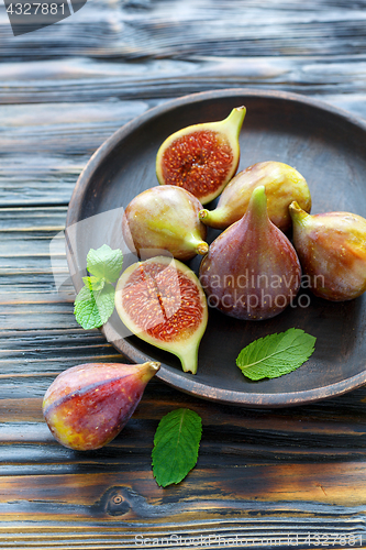 Image of Ripe figs and mint leaves on a wooden dish.