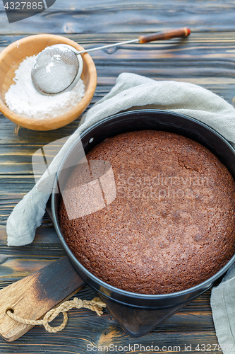 Image of Chocolate cake in a metal form and bowl with powdered sugar.