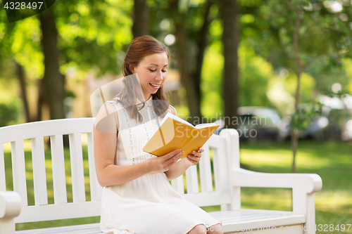 Image of smiling young woman reading book at summer park