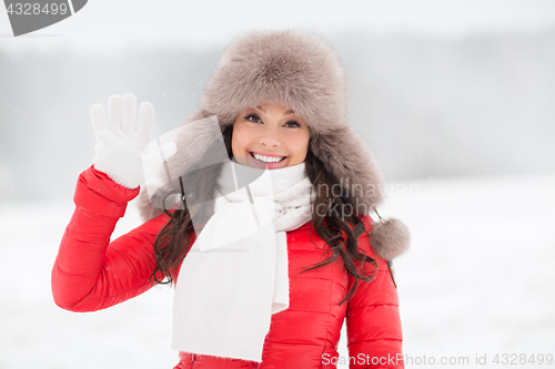 Image of happy woman in winter fur hat waving hand outdoors