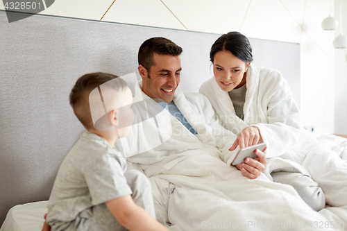 Image of happy family with smartphone in bed at hotel room