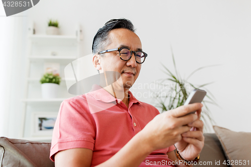 Image of asian man with smartphone sitting on sofa at home
