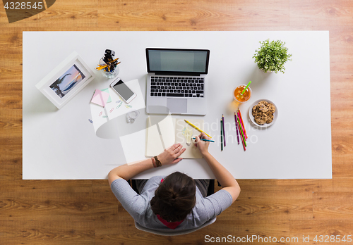 Image of woman with laptop drawing in notebook at office