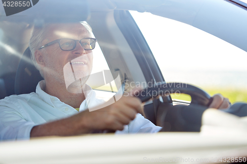 Image of happy senior man in glasses driving car