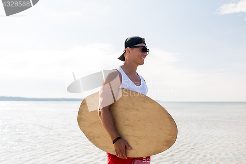 Image of happy young man with skimboard on summer beach