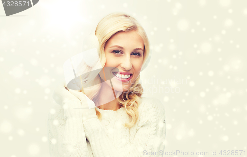 Image of smiling young woman in winter earmuffs and sweater