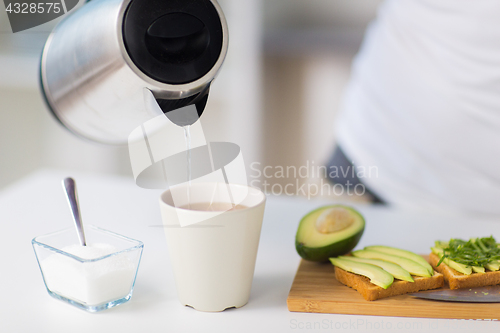 Image of kettle pouring hot water to tea cup at home