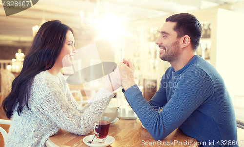 Image of happy couple with tea holding hands at restaurant