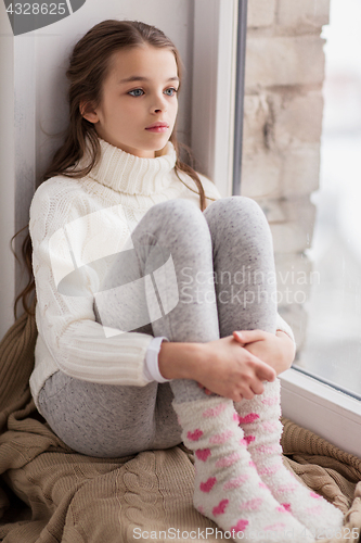 Image of sad girl sitting on sill at home window in winter