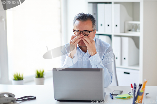 Image of tired businessman in glasses with laptop at office