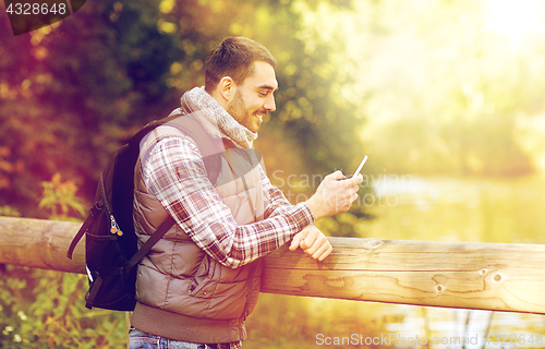 Image of happy man with backpack and smartphone outdoors