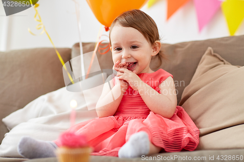 Image of happy baby girl looking at birthday cupcake