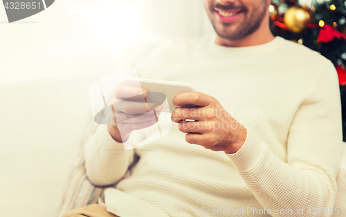 Image of smiling man with smartphone at home for christmas
