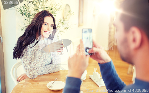 Image of man taking picture of woman by smartphone at cafe