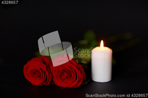 Image of red roses and burning candle over black background