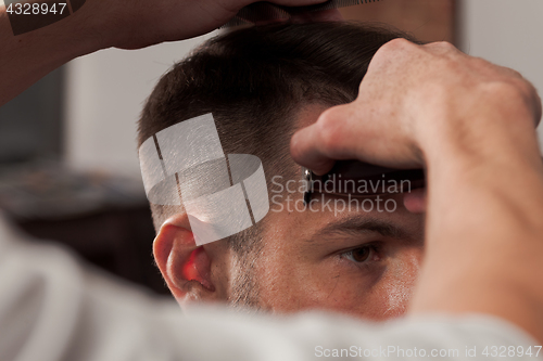 Image of The hands of barber making haircut to young man in barbershop