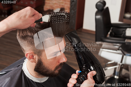 Image of The hands of barber making haircut to young man in barbershop