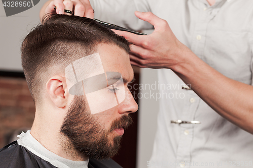 Image of The hands of barber making haircut to young man in barbershop