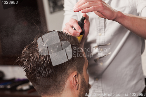 Image of The hands of barber making haircut to young man in barbershop