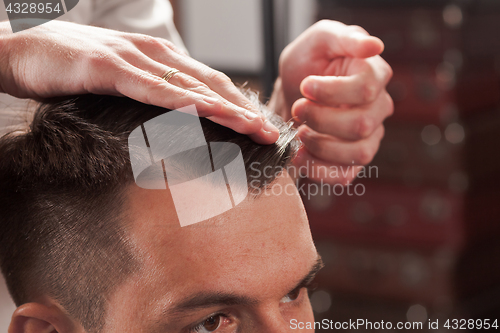 Image of The hands of barber making haircut to young man in barbershop