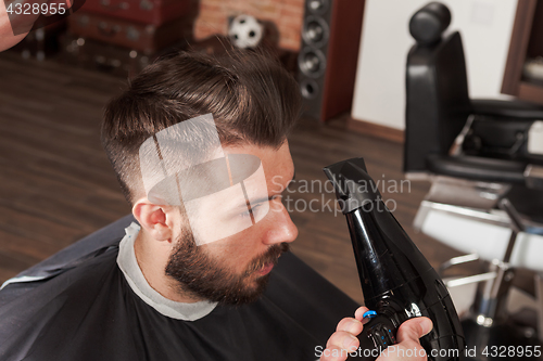 Image of The hands of barber making haircut to young man in barbershop