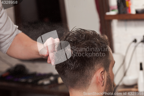 Image of The hands of barber making haircut to young man in barbershop